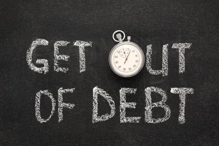 The words get out of debt are printed on a blackboard, with the O in the word out portrayed by a stopwatch.