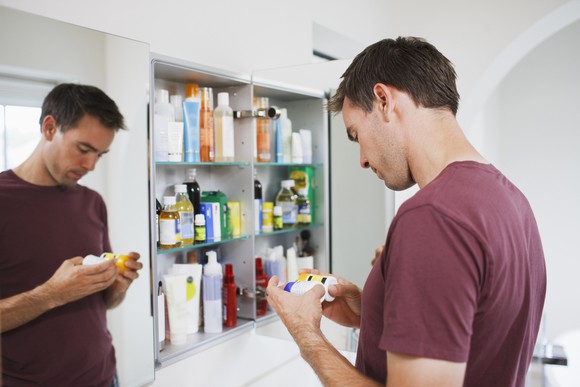 Man standing in front of medicine cabinet, holding pill bottles.