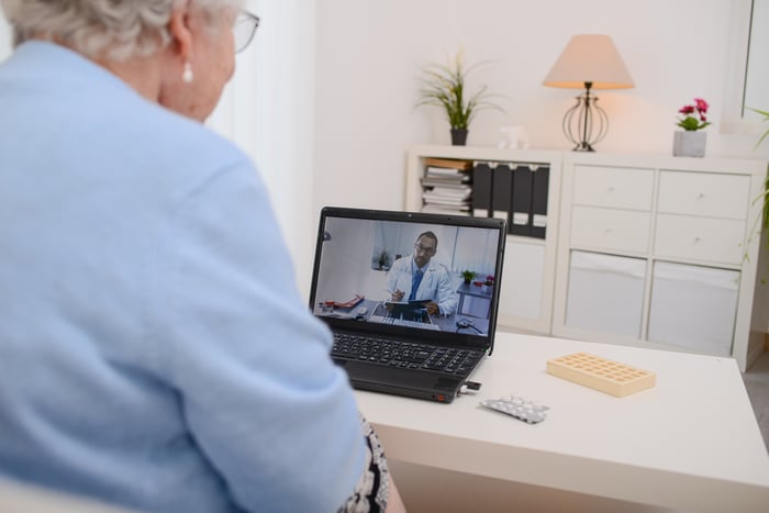 An elderly woman videoconferencing with a doctor on a laptop.