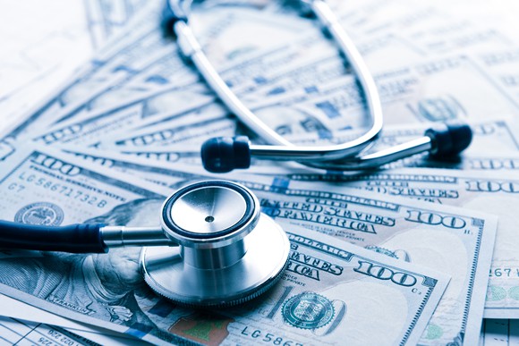 A stethoscope sitting on top of several one hundred dollar American bills.