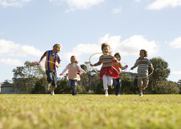 Five children with hula hoops running through a field.