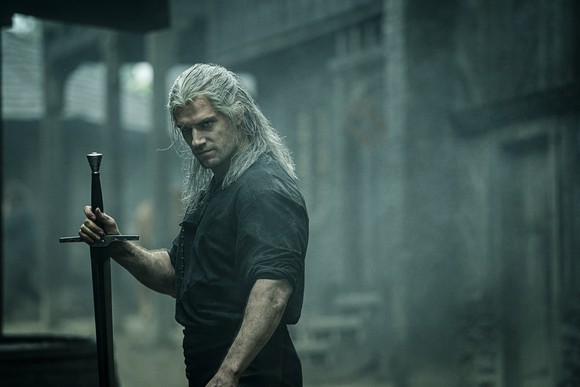 A muscular man with a serious gaze and long white hair holding a sword by the hilt