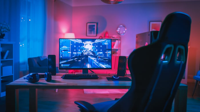 An at-home desk with a large gaming computer monitor glowing in the dark