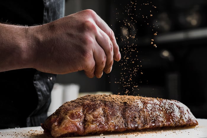 raw piece of meat with the hand of a chef adding spices