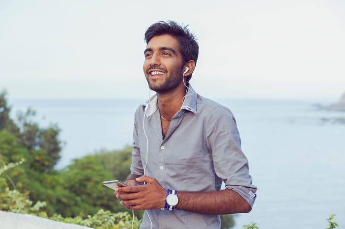 A young Indian man outside smiling while listening to music with headphones