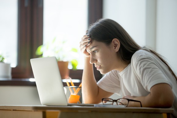 Young woman sitting at laptop, holding her head.