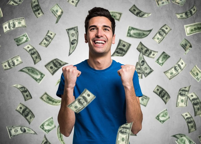 Man with huge smile and pumped fists as one hundred dollar bills rain all over him.  