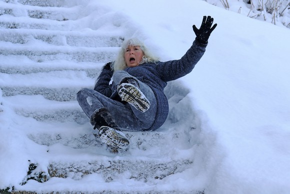 An older woman falling down a flight of snowy steps outdoors