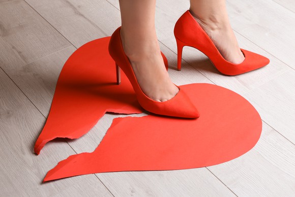 Woman in red high heels stepping on a broken heart.