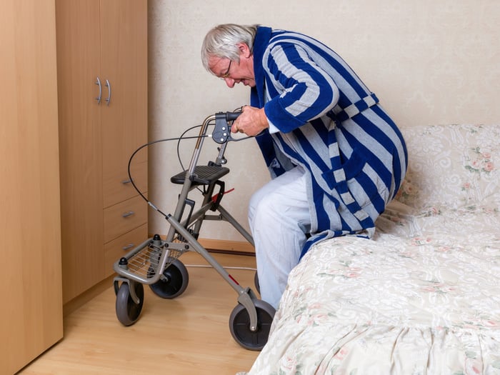 Man in bathrobe sitting on bed holding onto walker