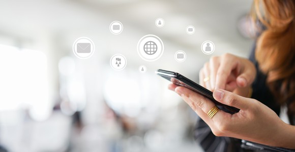 A person using a smartphone, with digital icons representing connectivity surrounding it