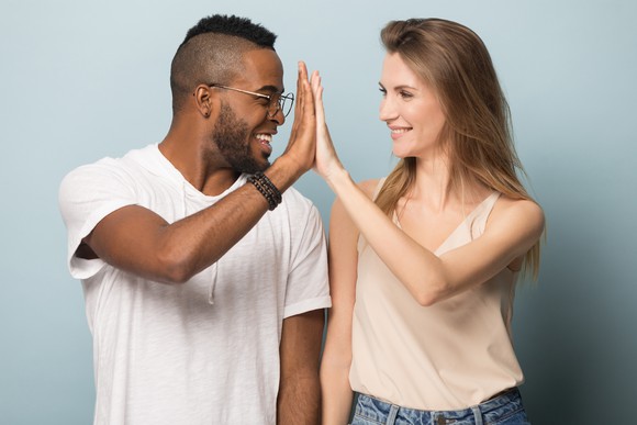 Young man and young woman looking at each other and high-fiving.