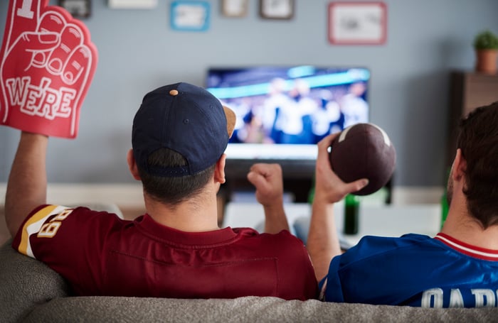 Two men sitting on a couch watching football on television.