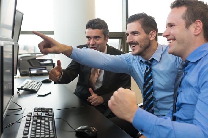 Three traders pointing at a computer screen and smiling