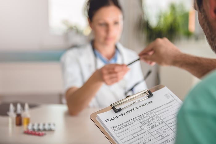 Woman handing man a clipboard with health insurance sign-up papers and a pen