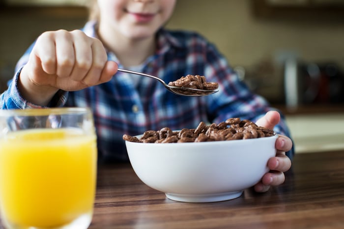 Close-up of a young girl eating chocolate cereal at breakfast.