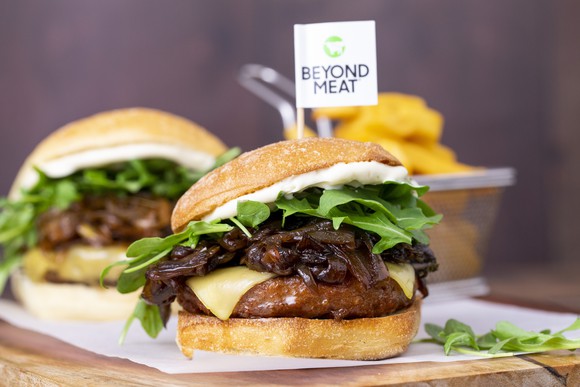 Two Beyond Meat burgers inside buns with cheese, greens, and onions.