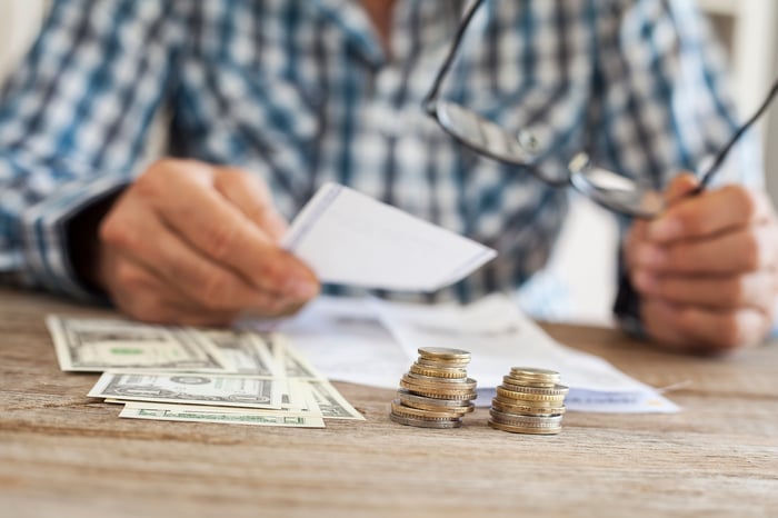 A man removing his glasses and looking at paperwork on the table near some cash and coins