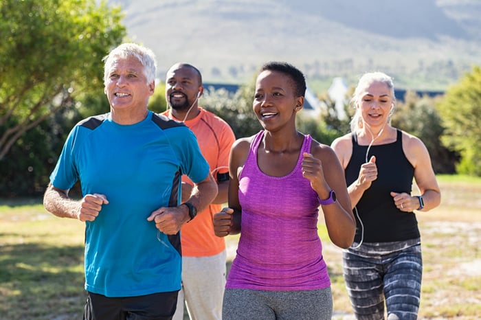 For middle-aged people -- a white woman, a black woman, a white man, and a black man -- running in a park during warm weather.