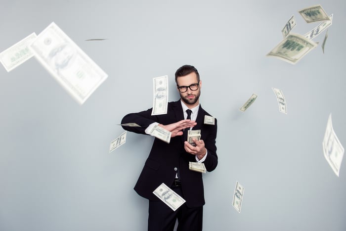 A man in a suit shooting hundred-dollar bills off of a pile in his hand.