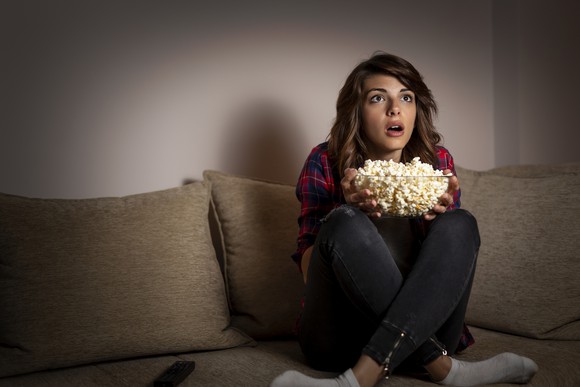 A girl sitting on the couch with a bowl of popcorn.
