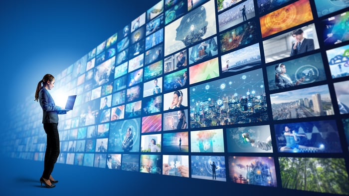 Woman with laptop standing in front of a wall of movie screens