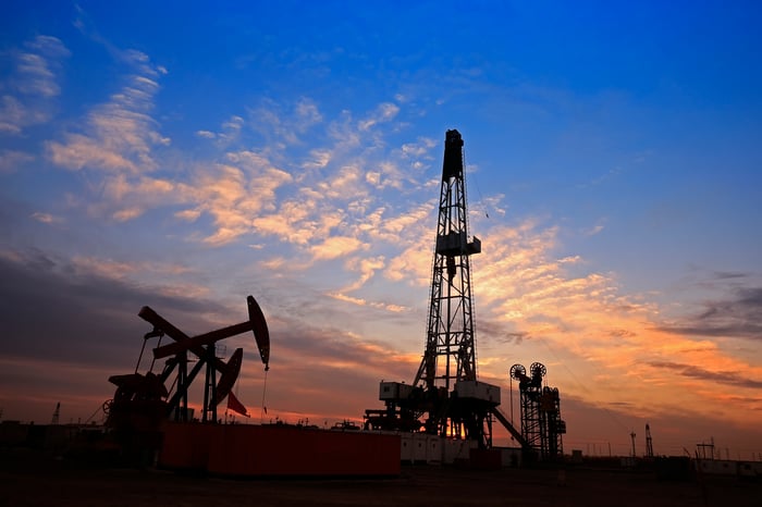 A drilling rig near some oil pumps with a nice sunset in the background.