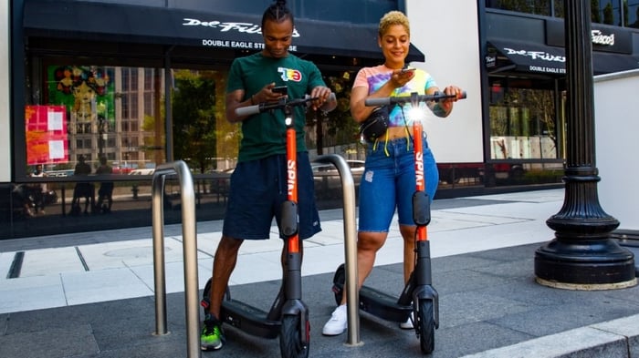 Two people standing on Spin scooters on a sidewalk