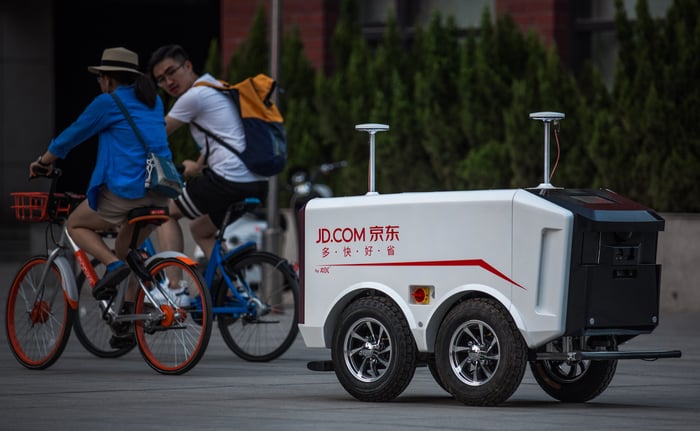 An autonomous delivery bot driving down a street with the JD.com logo displayed on the side.