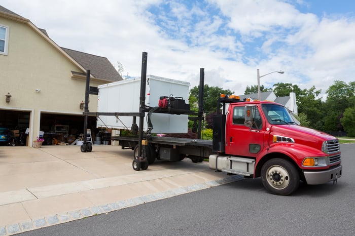 Portable storage container being delivered on the bed of a tractor-trailer