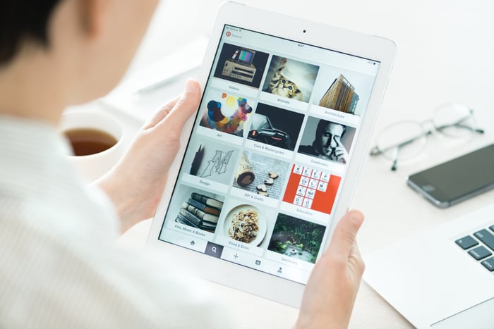 A woman's hands holding a white computer tablet showing several Pinterest categories on screen.