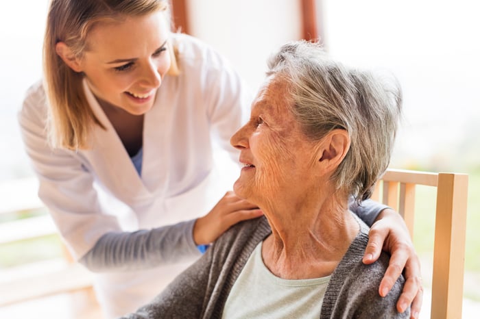 A young woman in a medical coat comforting an older woman sitting down