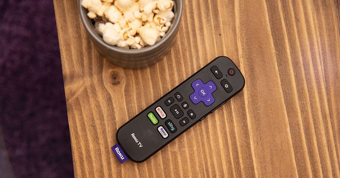 A Roku remote on a table next to a bowl of popcorn