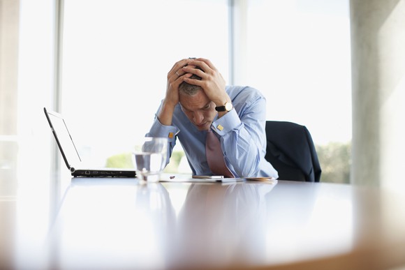 Man in shirt and tie, slumped with head in hands, looking worried.