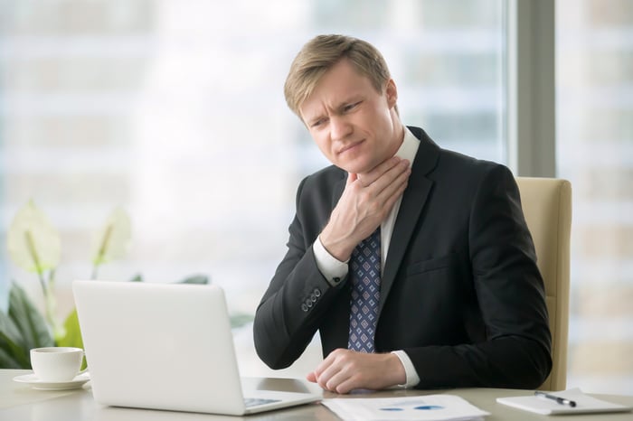 Man in suit at desk touching his neck