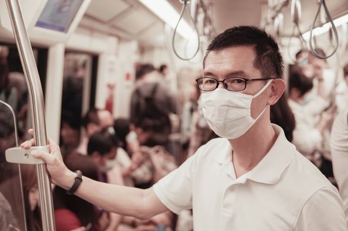 A young man wearing a surgical mask on a crowded train.