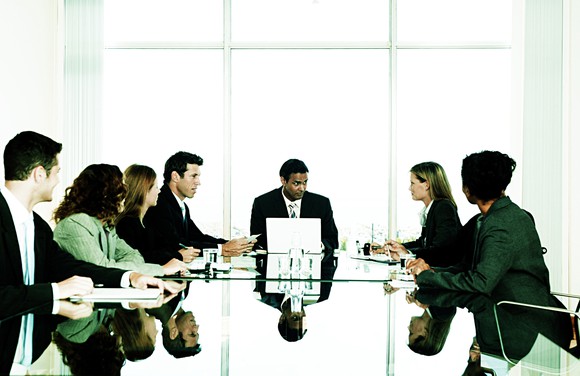 Office workers meet around a long boardroom table.