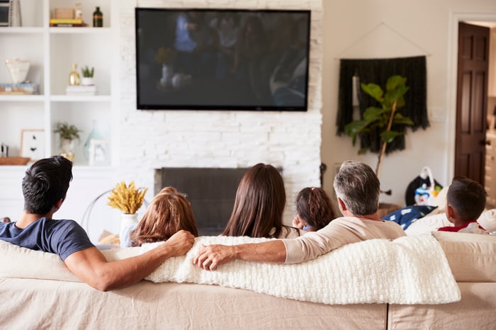 Several generations of a family sitting on a couch watching television.