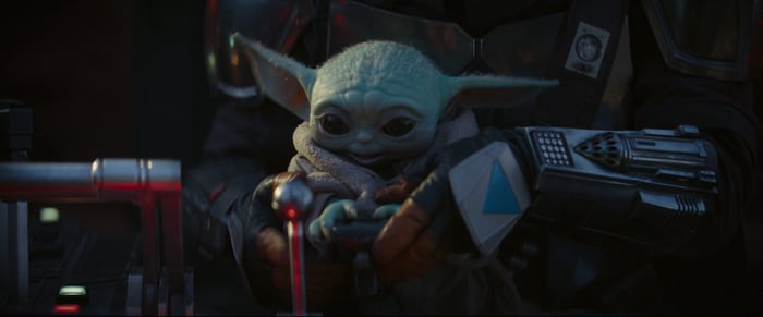 A small green alien with long pointy ears sitting on an unseen traveler's lap.