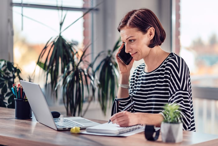 Woman talking on a smart phone and writing notes in notebook.
