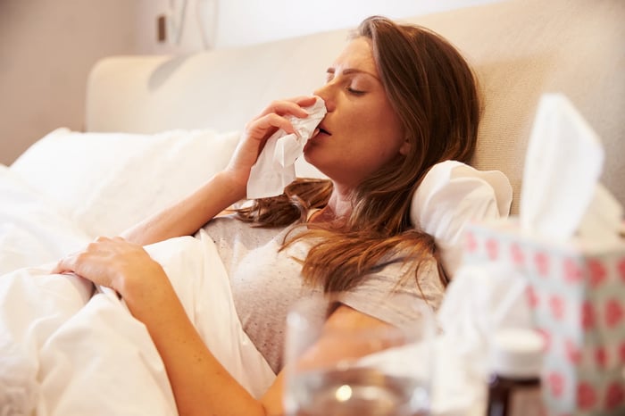 Person in bed with tissue on nose.