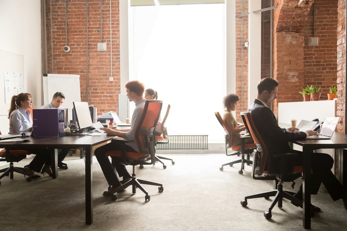 Workers at computers in a brick walled office space