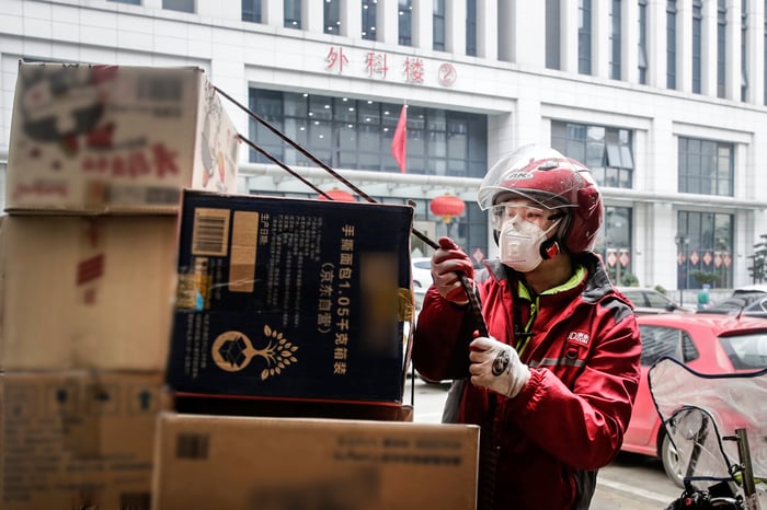 A JD delivery courier in a mask untethers boxes for delivery on the street.