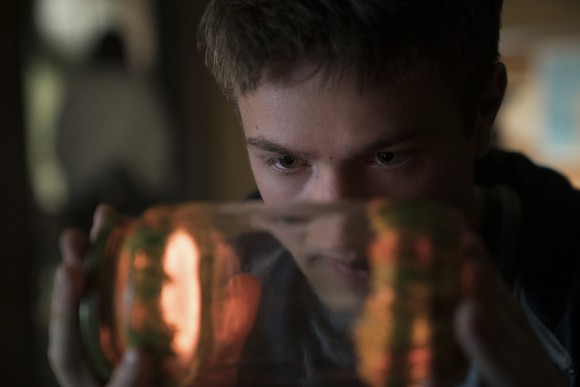 A young man looking at a glowing object in a jar.
