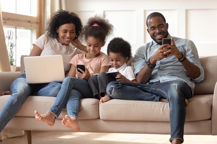 A family of four seated on the couch, with each person using a smartphone, laptop, or tablet.