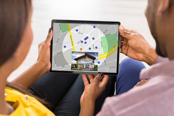 A couple looking at a tablet with a real estate app on it showing a map of homes