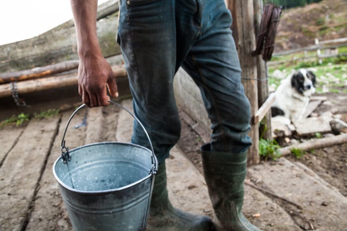A rancher in jeans and boots carrying a metal bucket