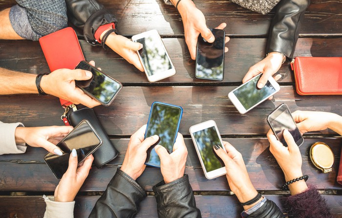 Multiple people holding their smartphones in a circle over a table.