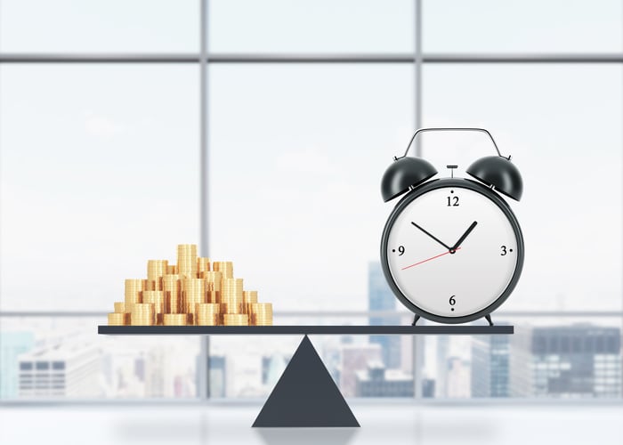 a clock balancing against a pile of coins on a seesaw