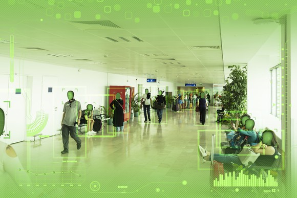 People walking through airport being watched via face recognition tech.